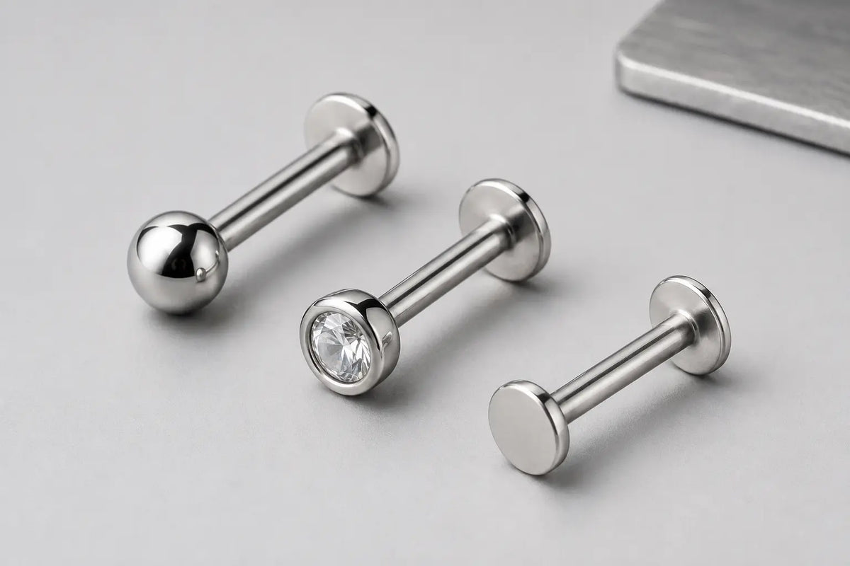 Illustrative close-up of polished titanium flat-back labrets showing the shafts, bases and surface finish.
