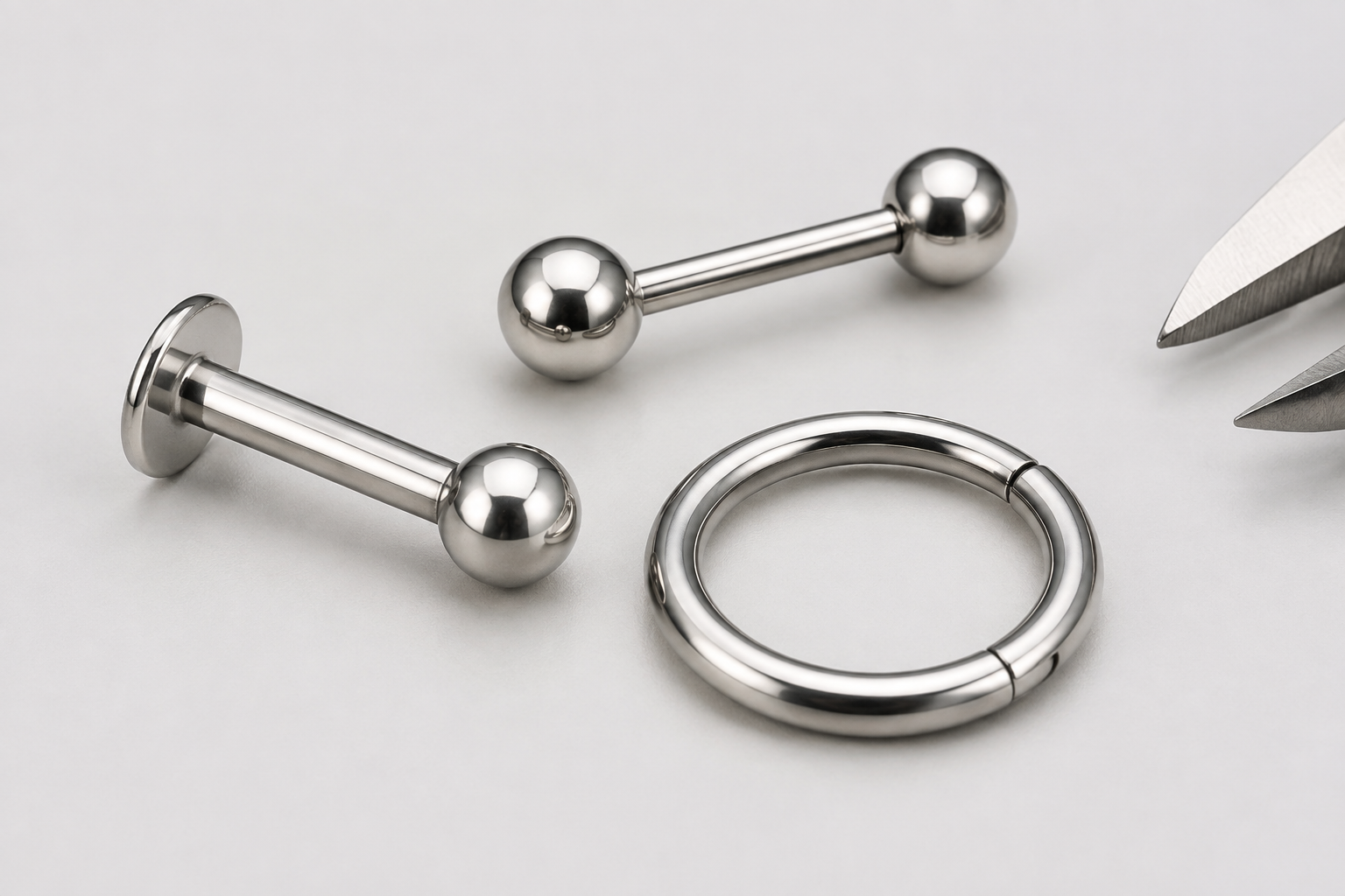 Close-up of a titanium labret, barbell and clicker ring with a small caliper detail for receiving inspection.