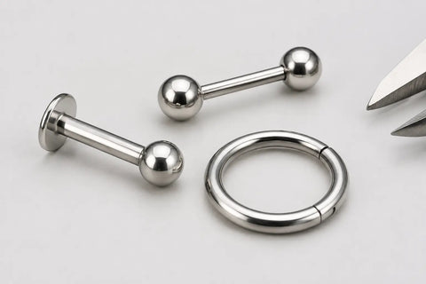Close-up of a titanium labret, barbell and clicker ring with a small caliper detail for receiving inspection.