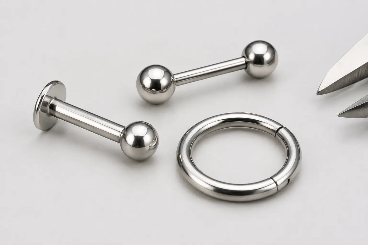 Close-up of a titanium labret, barbell and clicker ring with a small caliper detail for receiving inspection.