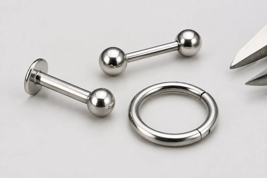 Close-up of a titanium labret, barbell and clicker ring with a small caliper detail for receiving inspection.